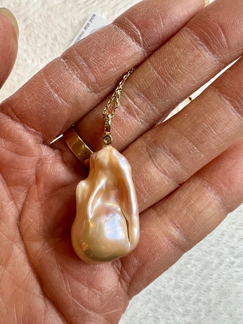 May include: A baroque pearl pendant necklace. The pendant is a large, irregularly shaped pearl with a creamy, iridescent surface. It hangs from a delicate gold chain with a small diamond accent.