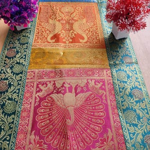 May include: A colorful textile table runner with a peacock design. The runner features a vibrant mix of colors, including green, blue, orange, yellow, and pink. The peacock design is in gold. The edges are decorated with floral patterns.