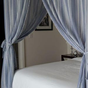 May include: A bed with a white mattress and a white valance. The bed is draped with blue and white striped fabric, creating a canopy effect. The fabric is tied back on each side.