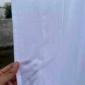Puede incluir: Primer plano de una tela blanca con un tejido texturizado. Una mano sostiene la tela, revelando el borde y la textura del material. El fondo está borroso.