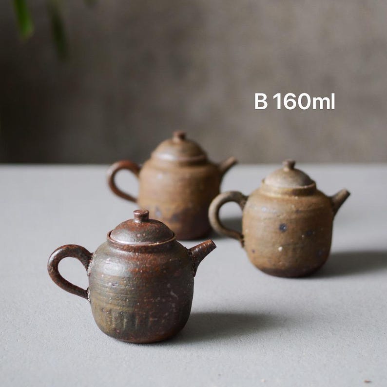 May include: Three brown ceramic teapots of varying sizes. The smallest teapot is in the foreground and the largest teapot is in the background. The teapots have a rustic, hand-crafted look. B 160ml.