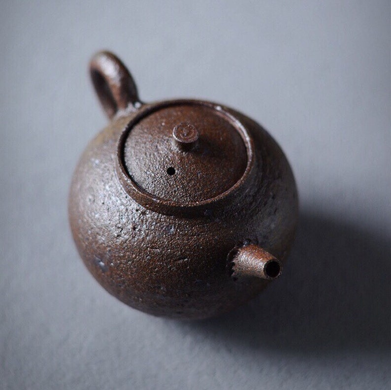 May include: A small, brown, ceramic teapot with a lid and a spout. The teapot has a rough, textured surface.