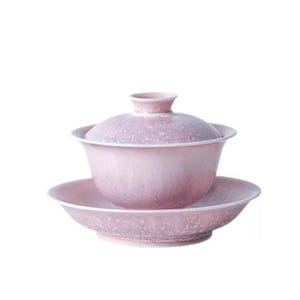 May include: A pink ceramic tea set with a lid, cup, and saucer. The set has a speckled texture and a soft, gradient color scheme. The tea set is designed for serving tea.