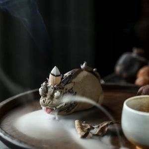 May include: A ceramic incense burner shaped like a mythical creature with a pointed horn on its head. The burner is emitting smoke, creating a mystical atmosphere.