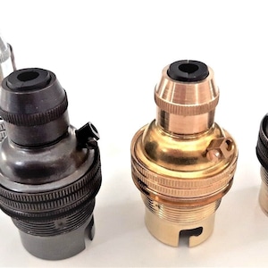 May include: Four different coloured light bulb sockets. The sockets are made of metal and have a black rubber ring around the top. The colours are silver, black, brass, and copper.