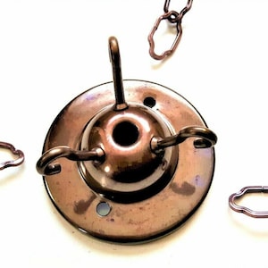 May include: A bronze ceiling fixture with three hooks for hanging light fixtures. The fixture has a round base and a central hole for attaching to a ceiling.
