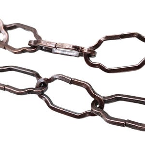 May include: A close-up of a brown metal chain with a decorative, octagonal link design.