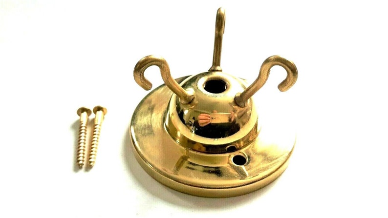 May include: A gold-toned metal ceiling fixture with three hooks and two screws. The fixture has a round base and a domed top.