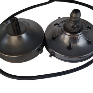 May include: Two metal ceiling fan light fixture parts in a dark bronze finish. One part has a round base with a centre hole and the other part has a decorative design with cutouts.