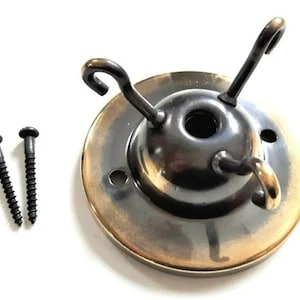 May include: A brass ceiling fixture with three hooks and two black screws. The fixture has a round base with a gold-colored rim.