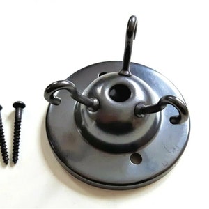 May include: Black metal ceiling fixture with three hooks and two screws. The fixture has a round base with a hole in the center.