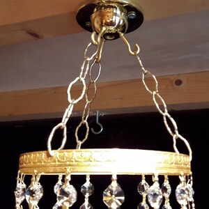 May include: Gold chandelier with a round crystal base and a chain hanging from a ceiling hook.
