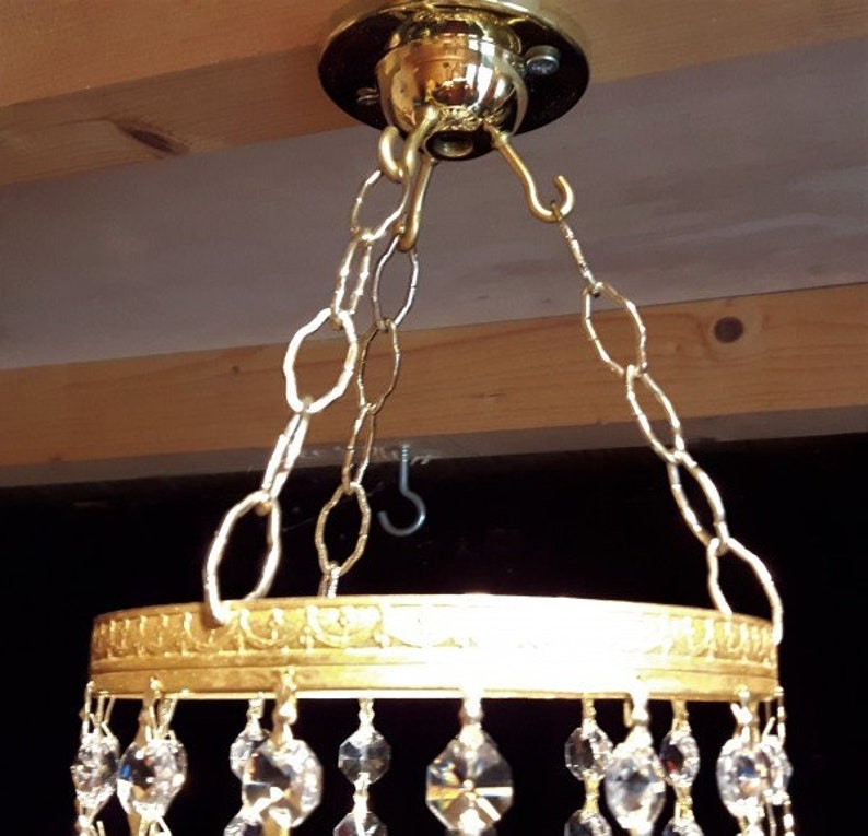 May include: Gold chandelier with a round crystal base and a chain hanging from a ceiling hook.