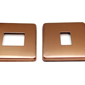 May include: Two brushed copper wall plate covers with rectangular cutouts for light switches.