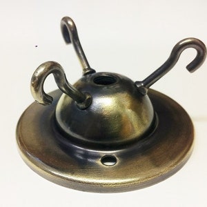 May include: A brass ceiling fixture with three hooks for hanging light fixtures. The fixture has a round base and a domed top.