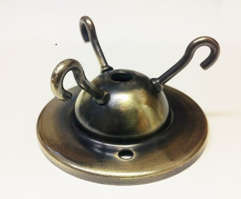 May include: A brass ceiling fixture with three hooks for hanging light fixtures. The fixture has a round base and a domed top.
