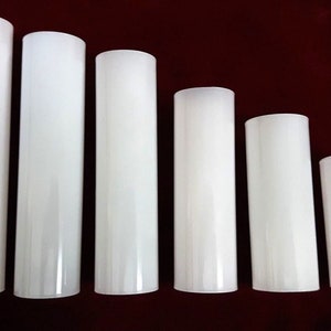 May include: Six white cylindrical glass candle holders of varying sizes. The holders are arranged in a row from largest to smallest.
