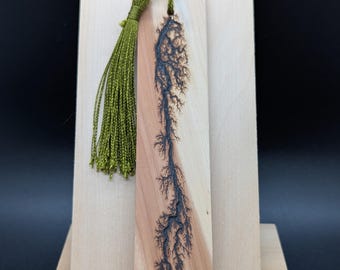 Könnte beinhalten: Holzlesezeichen mit einem dunklen, baumartigen Design, das in das Holz gebrannt wurde. Das Lesezeichen hat eine grüne Quaste oben. Das Holz hat eine natürliche, hellbraune Farbe.