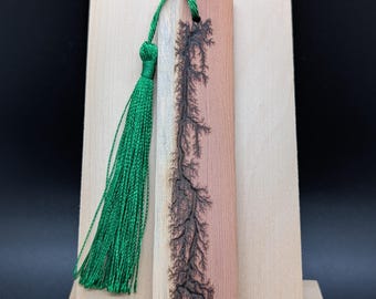 Könnte beinhalten: Ein hölzernes Lesezeichen mit einem detaillierten, dunkelbraunen baumartigen Design. Das Lesezeichen ist rechteckig mit natürlicher Holzmaserung und einer grünen Quaste. Das Design ist auf dem Lesezeichen zentriert.