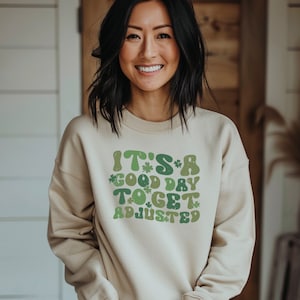 Peut inclure: Un sweat-shirt beige avec un motif vert et blanc qui dit "C'est un bon jour pour s'ajuster".