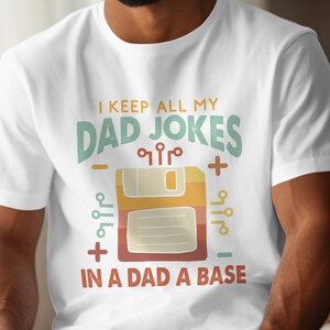Könnte beinhalten: Weißes T-Shirt mit einer Retro-Grafik einer Diskette und dem Text "I keep all my dad jokes in a dad a base".