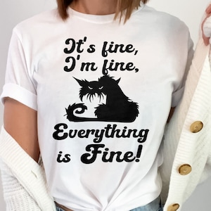 May include: White t-shirt with a black silhouette of a cat and the text "It's fine, I'm fine, Everything is Fine!"