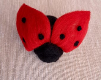 Könnte beinhalten: Eine handgefertigte Marienkäfer-Figur aus rotem und schwarzem Filz. Der Marienkäfer hat rote Flügel mit schwarzen Punkten und einen schwarzen Körper. Der Filz ist strukturiert und der Marienkäfer liegt auf einer hellbraunen Oberfläche.