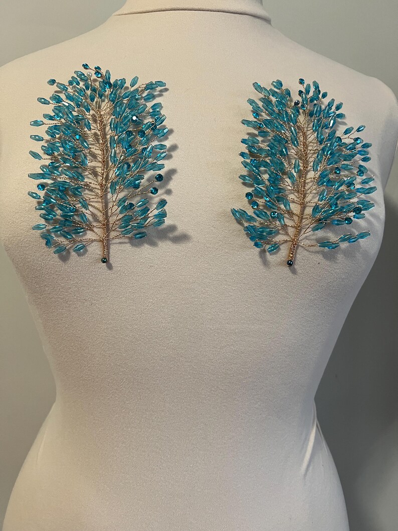 May include: Two teal beaded hair accessories in a tree branch design. The branches are made of gold wire and are adorned with numerous teal-colored beads. The accessories are displayed on a white mannequin.