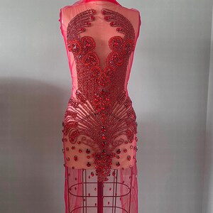 May include: A red sheer dress with a beaded design. The beads are arranged in a pattern of flowers and leaves. The dress is on a mannequin.