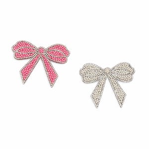 May include: Two decorative bow-shaped brooches. One is pink with a beaded design and silver-colored trim. The other is white with a pearl-like beaded design and silver-colored trim. Both are set against a white background.