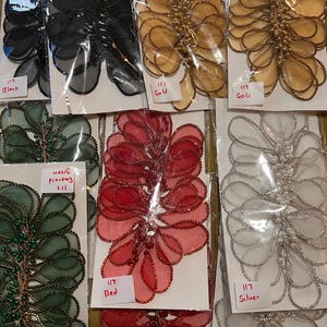 May include: Assortment of 117 decorative embellishments in various colours, including black, gold, red, green, and silver. Each embellishment is made of a delicate, layered fabric with a beaded edge.