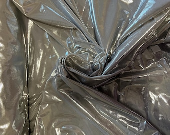 May include: Silver metallic fabric with a shiny, iridescent finish. The fabric is folded and draped, showcasing its texture and drape.