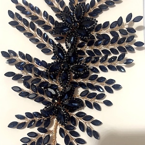 K&ouml;nnte beinhalten: Ein dekoratives Haaraccessoire mit einem symmetrischen Design aus marineblauen Kristallbl&auml;ttern und floralen Clustern. Die Kristalle sind auf einer goldfarbenen Metallbasis angebracht, was einen funkelnden, eleganten Look erzeugt. Geeignet f&uuml;r besondere Anl&auml;sse.