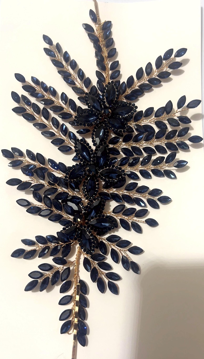 K&ouml;nnte beinhalten: Ein dekoratives Haaraccessoire mit einem symmetrischen Design aus marineblauen Kristallbl&auml;ttern und floralen Clustern. Die Kristalle sind auf einer goldfarbenen Metallbasis angebracht, was einen funkelnden, eleganten Look erzeugt. Geeignet f&uuml;r besondere Anl&auml;sse.