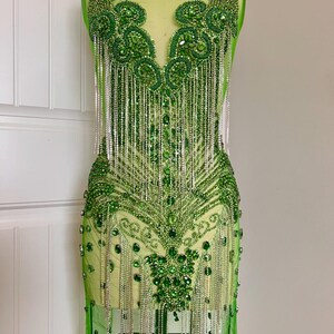 Puede incluir: Un corpiño verde con cuentas y lentejuelas con flecos. El corpiño está en un maniquí y está hecho de tela transparente.