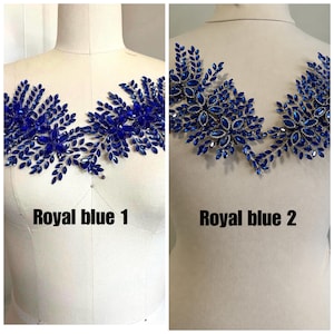 K&ouml;nnte beinhalten: Zwei k&ouml;nigsblaue, mit Perlen besetzte Applikationen, beschriftet mit "Royal blue 1" und "Royal blue 2". Die Applikationen werden auf Schneiderpuppen pr&auml;sentiert. Die Applikationen weisen ein Blumen- und Bl&auml;tterdesign mit funkelnden blauen Perlen auf.