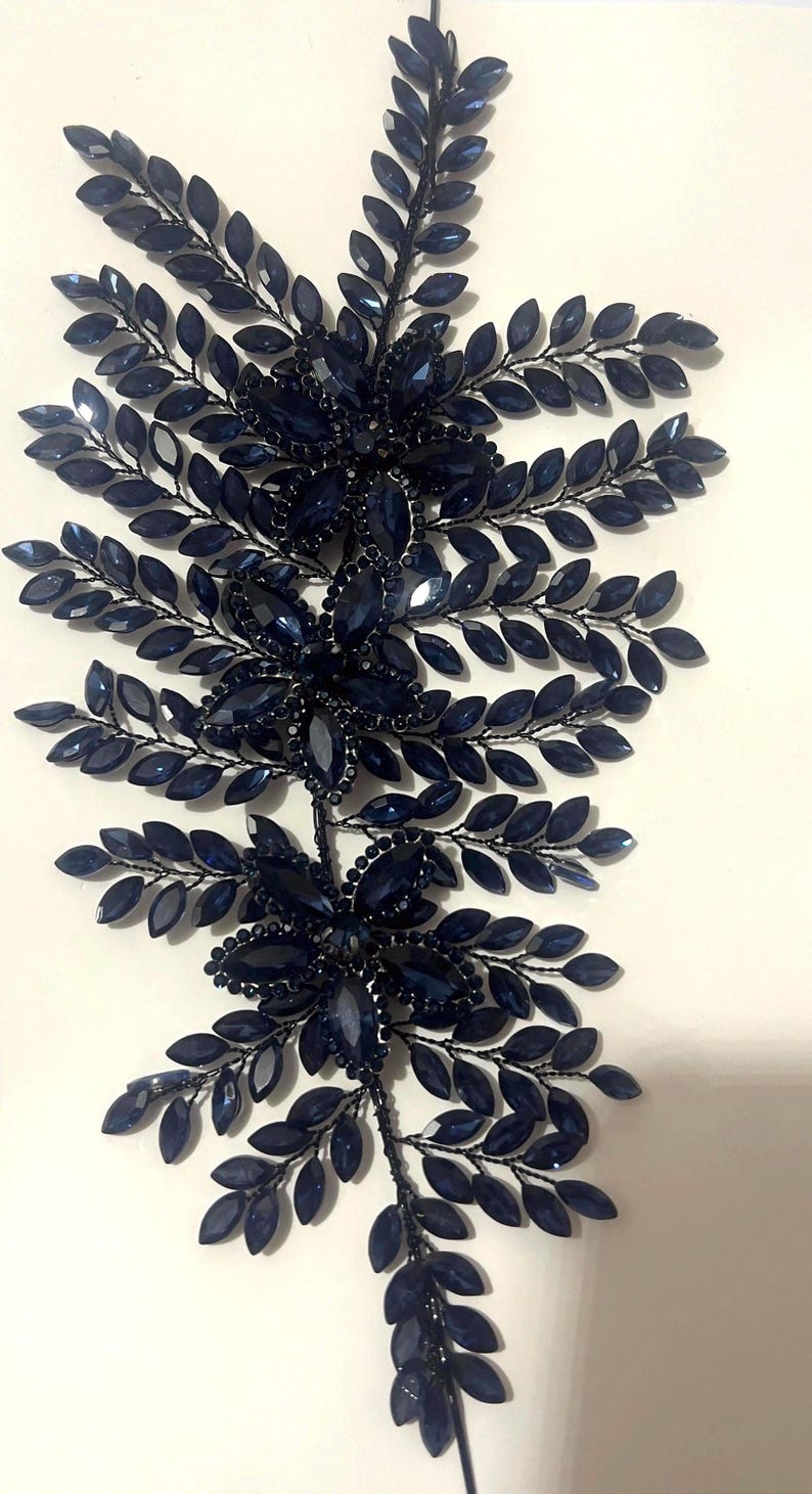K&ouml;nnte beinhalten: Dunkelblaues Haaraccessoire mit floralem und Bl&auml;tter-Design. Es zeigt Gruppen dunkelblauer Juwelen und blattf&ouml;rmige Akzente, alle auf einem schwarzen Drahtrahmen. Das Design ist symmetrisch und elegant, ideal f&uuml;r besondere Anl&auml;sse.