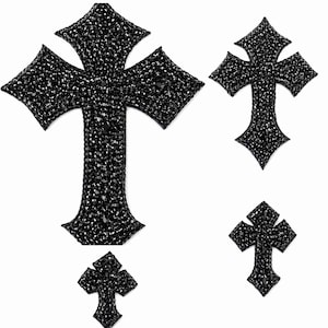May include: Four black cross-shaped embellishments, each covered in small, sparkling black rhinestones. The crosses vary in size, with the largest at the top and the smallest at the bottom. The crosses are set against a white background.