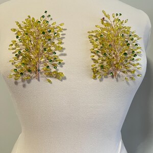 May include: Two decorative floral appliques. Each applique features a branch-like design crafted with yellow and green beads. The beads are attached to a thin, gold-colored wire frame. The appliques are displayed on a white mannequin.
