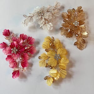 May include: Four floral hair accessories in white, gold, pink, and yellow. Each features delicate petal designs, crystal accents, and gold wire detailing. These decorative hair clips are ideal for weddings, proms, or special occasions.