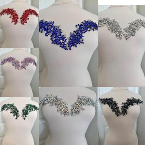 May include: A collection of decorative bodice appliques in various colors, including red, blue, silver, purple, green, iridescent, and black. Each applique is designed with a V-shaped pattern, featuring clusters of sparkling embellishments.