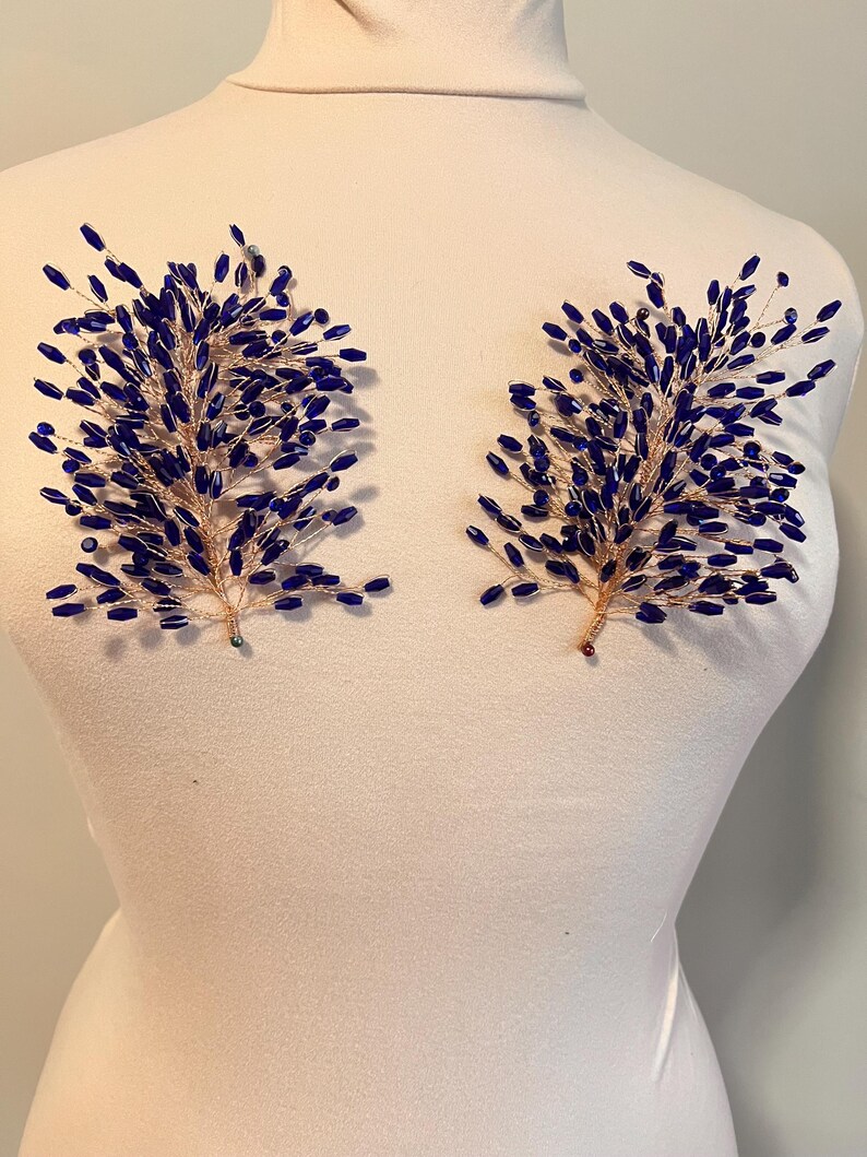 May include: Two decorative floral hair accessories. Each features a gold-toned wire base with clusters of dark blue beads, resembling stylized branches. The accessories are displayed on a white mannequin, showcasing their design and form.