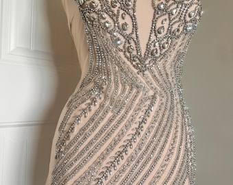 May include: A beaded embellishment for clothing, featuring a silver and clear crystal design. The embellishment is shaped like a V-neckline and has a fringe detail at the bottom.