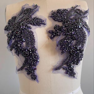 Op de afbeelding: Twee paarse parel-applicaties met een bloemmotief op een witte paspop.