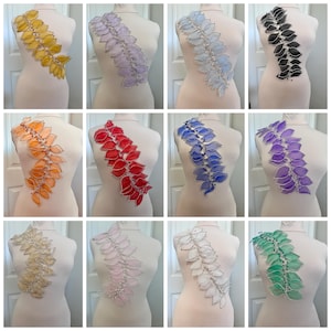 May include: A selection of decorative appliques in a range of colours: yellow, lavender, light blue, black, orange, red, blue, purple, beige, pink, white, and green. Each applique has a leaf-like design with beaded accents and silver trim, displayed on a mannequin.