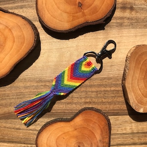 May include: Rainbow colored friendship bracelet keychain with a silver key ring and a tassel. The keychain is made with colorful embroidery floss.