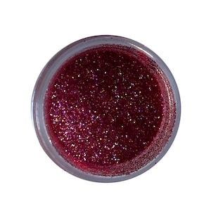 Puede incluir: Un tarro de plástico transparente lleno de purpurina burdeos brillante. La purpurina tiene una textura fina y refleja la luz, creando un efecto brillante. El tarro se ve desde arriba sobre un fondo blanco.