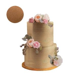 May include: A two-tiered gold-colored cake with floral decorations. The cake is adorned with pink and peach-colored roses, greenery, and a small, round sample of the cake's texture. The cake sits on a round, wooden base.