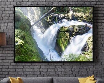 May include: A framed photograph of a waterfall cascading down a mossy rock face in a lush green forest. The water is flowing rapidly and creates a sense of movement and energy. The photograph is displayed on a gray brick wall above a gray sofa with yellow throw pillows.