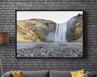 May include: A framed photograph of a waterfall cascading down a rocky cliffside. The photo is hanging on a gray brick wall above a gray sofa with yellow throw pillows.